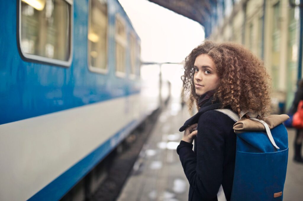 A young woman with curly hair waits at a train station with her backpack.